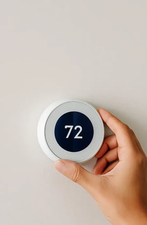 Hand adjusting a smart thermostat for demand response enrollment.